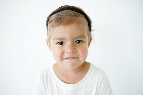Girl toddler wearing black headband on a white background for daycare school picture